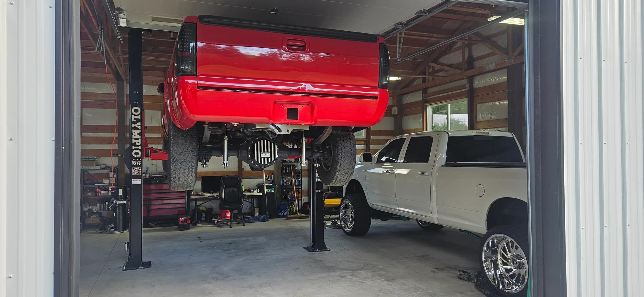 Red pickup raised on a two-post automotive lift inside a workshop